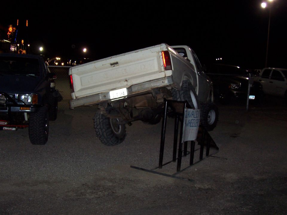 Lifted white Ford pickup parked rear-up on a ramp stand at night in a gravel lot