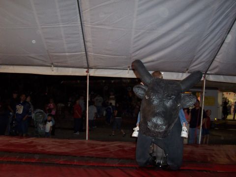 1981 Ford F-150 - A mechanical bull ride is set up under a tent at an event, with a child riding on top.