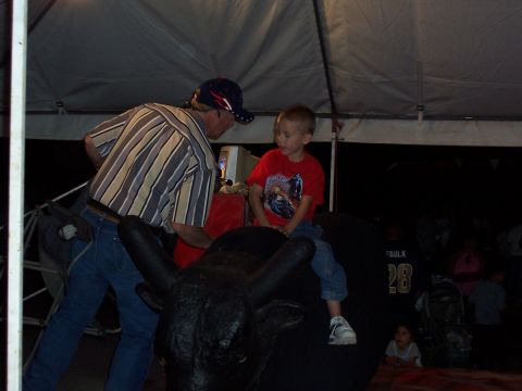 1981 Ford F-150 - A boy rides a mechanical bull with an adult's assistance at an event.