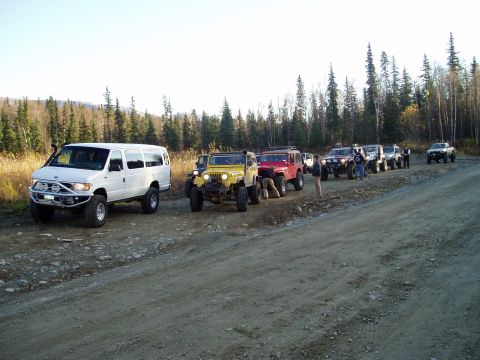 2000 Ford E350 - A group of off-road vehicles, including a van and several Jeeps, are lined up on a dirt road in a wooded area.