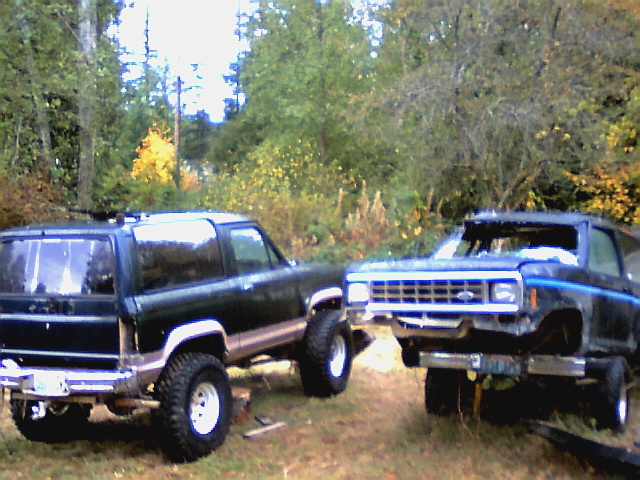 Two dark-colored Ford Bronco II SUVs parked outdoors, one with its front end elevated