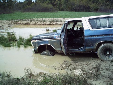 1986 Ford Bronco - Ford Bronco stuck in a muddy field with the driver's door open.