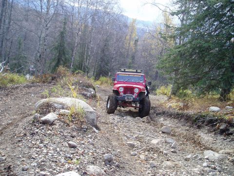 2000 Ford E350 - A red Jeep navigates a challenging off-road path through a forest.