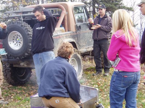 2000 Ford E350 - A group of people gather around a muddy Jeep Wrangler in an outdoor setting.