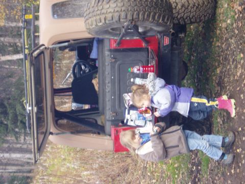 2000 Ford E350 - Two children are gathered around the open tailgate of a tan Jeep Wrangler, with a spare tire mounted on the back.