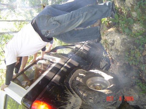 1986 Ford Bronco - An off-road SUV is stuck on rocks, with people attempting to get out or assist.