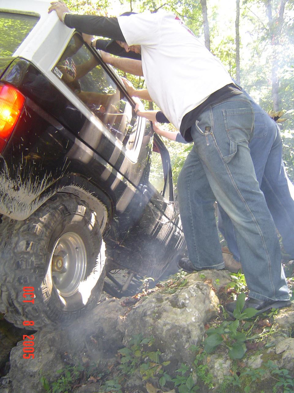 Black SUV stuck on rocks, people pushing it