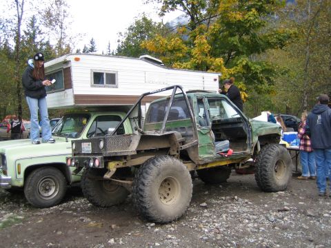 1990 Ford Bronco - Two trucks are parked side-by-side, one with a camper and the other heavily modified for off-roading.