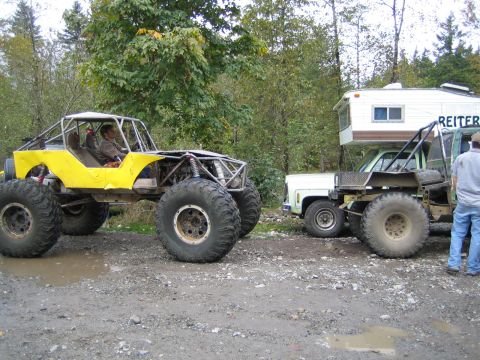 1990 Ford Bronco - Two custom vehicles, one a buggy and the other a tow truck, are parked on a dirt road with trees in the background.