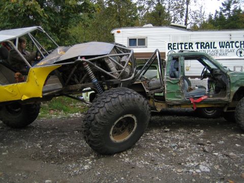 1990 Ford Bronco - Custom off-road vehicles parked outdoors with a trailer in the background.