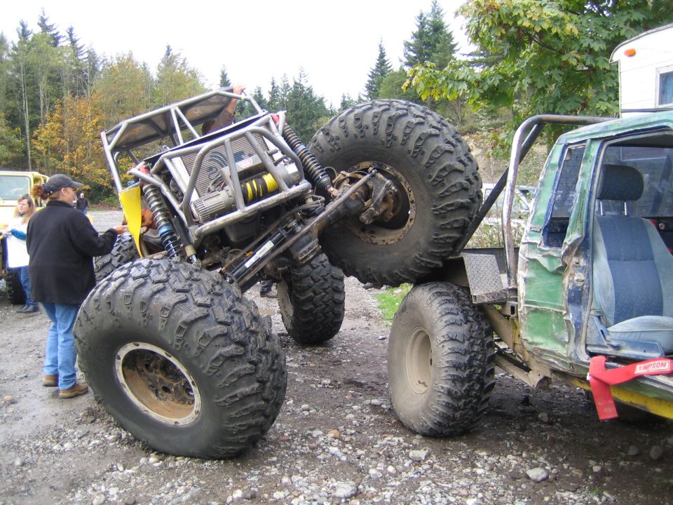 Two heavily modified off-road vehicles with large tires on a gravel surface