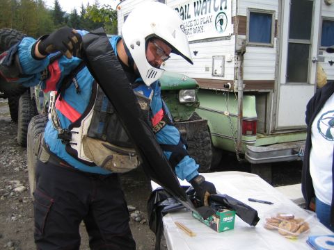 1990 Ford Bronco - A person in protective gear prepares equipment near a green truck and camper, possibly for an off-road event.