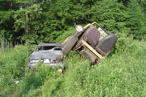 1987 Suzuki Samurai - Two vehicles are crashed and overgrown with weeds in a wooded area.