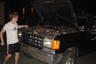 1987 Suzuki Samurai - A young man stands next to a black 1987 Suzuki Samurai with its hood open, revealing the engine compartment.