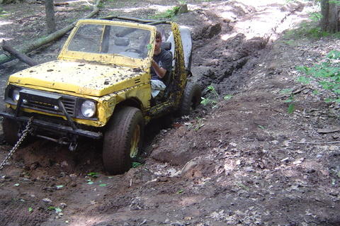 1987 Suzuki Samurai - A yellow 1987 Suzuki Samurai is stuck in a muddy off-road trail, with a person inside.