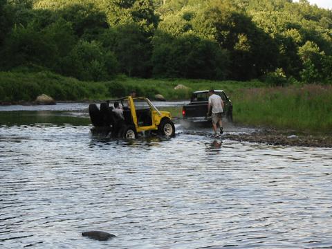 1987 Suzuki Samurai - A pickup truck tows a yellow off-road vehicle through a shallow body of water.