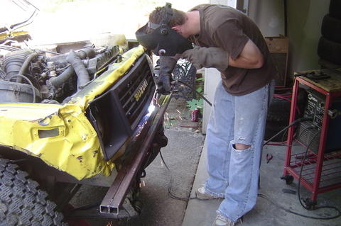 1987 Suzuki Samurai - A person welds the damaged front end of a yellow 1987 Suzuki Samurai in a workshop.