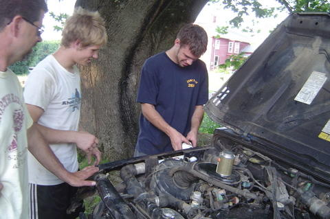 1987 Suzuki Samurai - Three men are gathered around the open hood of a vehicle, appearing to inspect the engine.