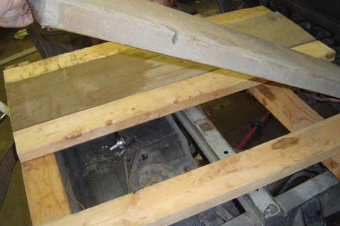 1987 Suzuki Samurai - Wooden planks obscure the view of a vehicle's underbody, revealing only a red pipe.