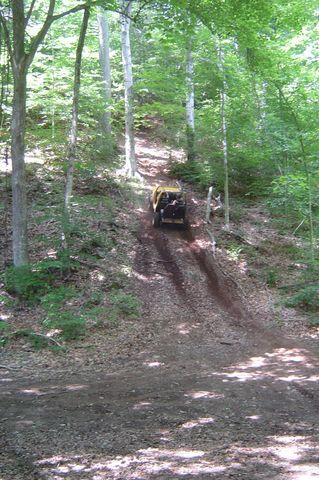 1987 Suzuki Samurai - Off-road vehicle navigates a challenging incline on a wooded trail.