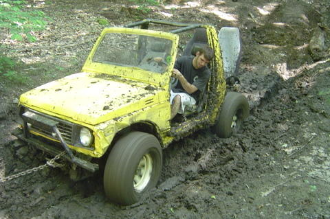 1987 Suzuki Samurai - A yellow off-road vehicle is stuck deep in the mud on a trail.