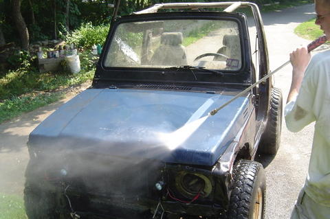 1987 Suzuki Samurai - A person pressure washes a blue 1987 Suzuki Samurai on a dirt road.