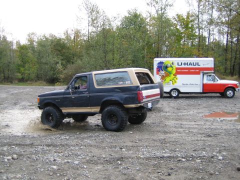 1990 Ford Bronco - A lifted Ford Bronco splashes through a muddy area next to a U-Haul truck.