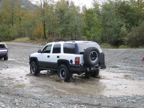 1990 Ford Bronco - This SUV is navigating through a muddy area with trees in the background.