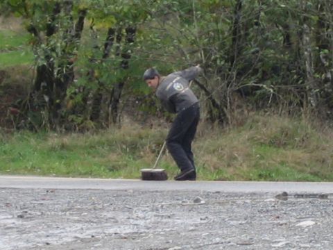 1990 Ford Bronco - Man sweeps the road surface, with trees and grass visible in the background.