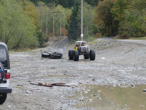 1990 Ford Bronco - An off-road buggy pulls a load of trash across a muddy, gravelly terrain with trees in the background.