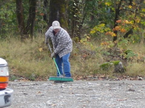 1990 Ford Bronco - A person sweeps a gravel area in a wooded setting, with part of a vehicle visible on the left.