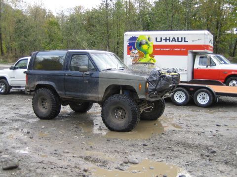 1990 Ford Bronco - A heavily modified Ford Bronco sits in a muddy lot next to a U-Haul truck and trailer.