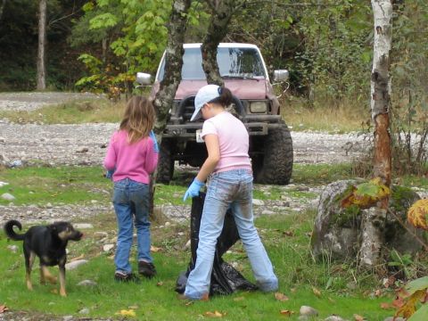 1990 Ford Bronco - Two children and a dog participate in a cleanup near a red SUV with large tires.