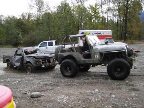 1990 Ford Bronco - A heavily damaged pickup truck sits in mud beside a lifted Jeep, with a U-Haul truck visible behind them.