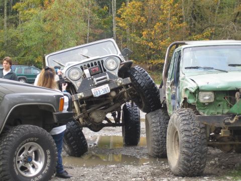 1990 Ford Bronco - A modified Jeep CJ-5, equipped with a winch and custom bumper, is positioned precariously between two other off-road vehicles.