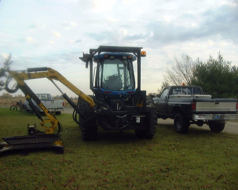 Pickup truck parked next to a blue tractor with an excavator attachment. The truck has a toolbox in the bed