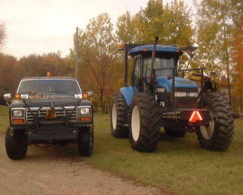 1985 Ford F-150 - A black 1980s Ford F-150 sits beside a large blue tractor on a grassy area.