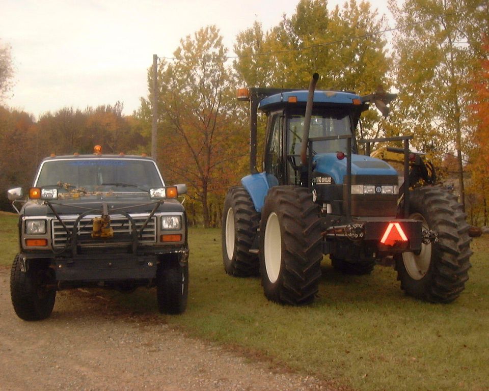 Black Ford F-150 with a brush guard and auxiliary lights, parked next to a blue tractor