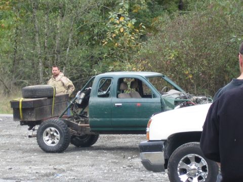 1990 Ford Bronco - A modified green pickup truck sits beside a white truck in an outdoor setting.