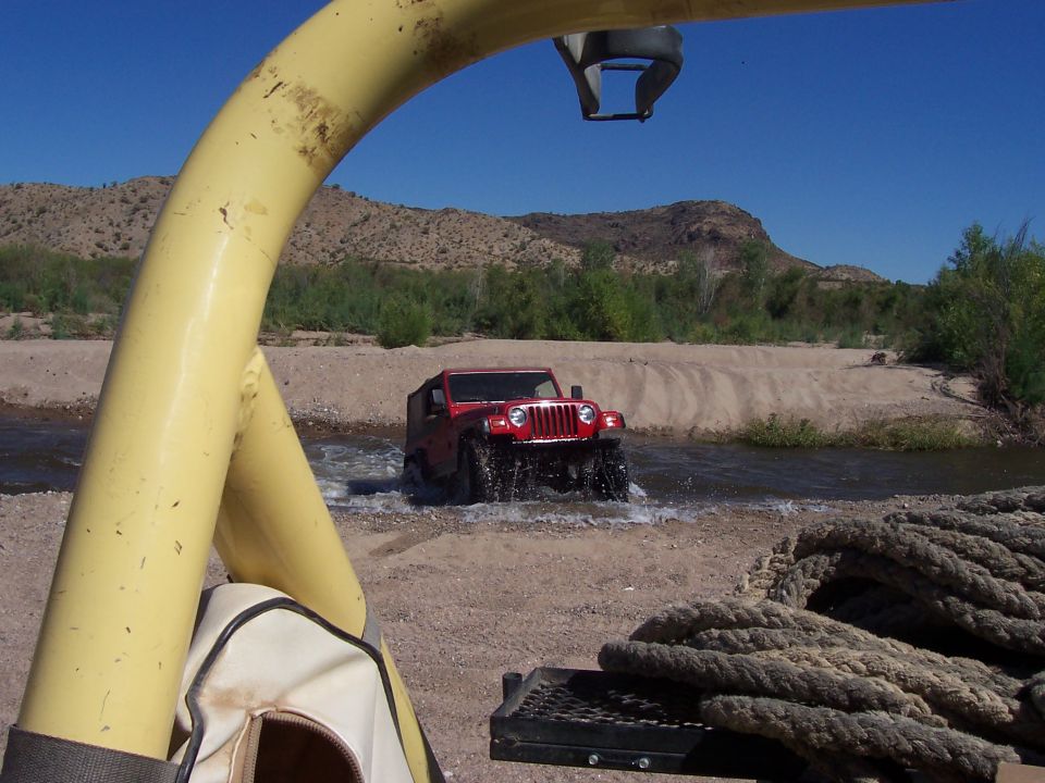 Red Jeep Wrangler driving through a river. Shot from inside another vehicle
