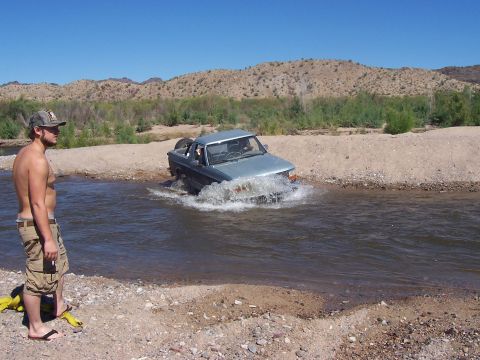 1996 Ford Bronco - A man watches a light blue pickup truck drive through a shallow river in a desert landscape.