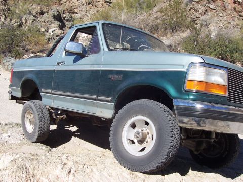 1996 Ford Bronco - A two-tone green and light blue 1996 Ford Bronco is shown off-road on a rocky trail.