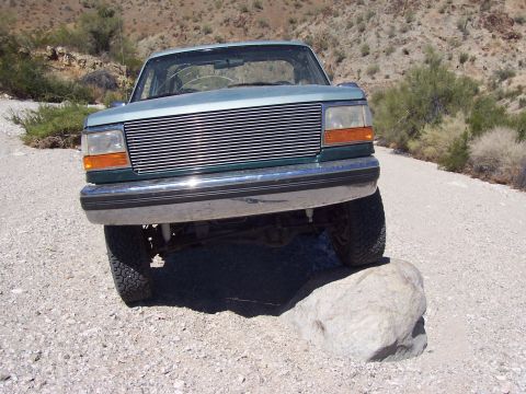 1996 Ford Bronco - This SUV is navigating a rough, rocky terrain with sparse desert vegetation.