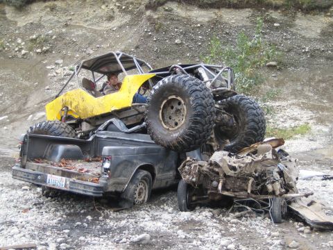 1990 Ford Bronco - A yellow off-road buggy is precariously balanced on top of a pickup truck in a rocky, outdoor setting.