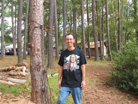 1966 Ford Ranchero - Man in t-shirt with Native American graphic in a wooded area with cabins and a "SUPERMOTORS.NET" logo.