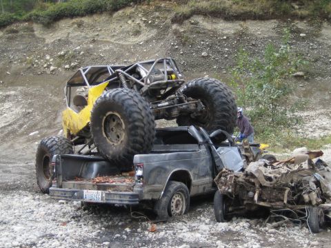1990 Ford Bronco - An off-road buggy is precariously balanced on a damaged pickup truck, with another severely damaged vehicle nearby.