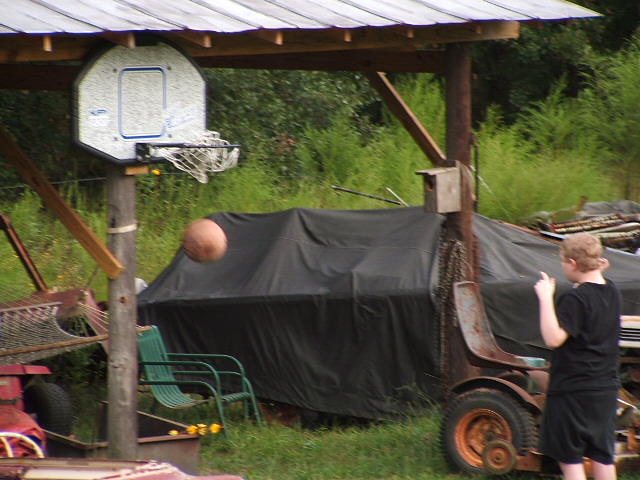 Vehicle covered by black tarp, with a basketball hoop and a person in the foreground