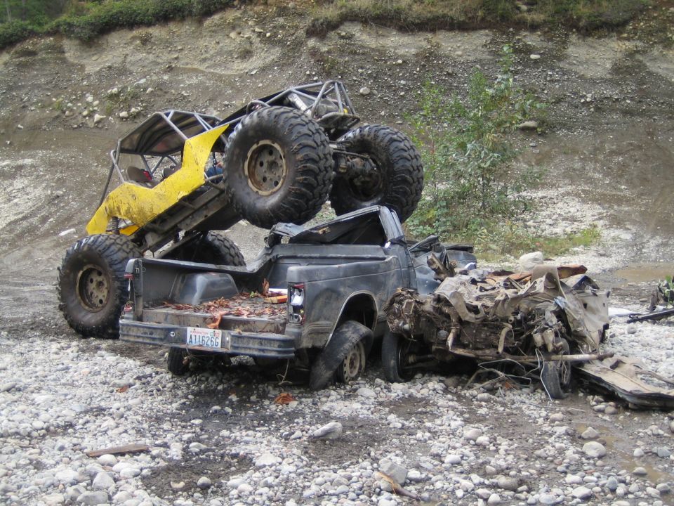 Yellow off-road buggy on top of a wrecked pickup truck. Pickup truck is heavily damaged