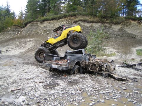 1990 Ford Bronco - A yellow off-road buggy is perched on a heavily damaged pickup truck in a muddy, rocky area.
