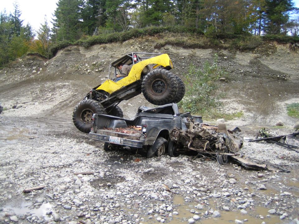 Yellow buggy atop wrecked pickup truck in rocky terrain